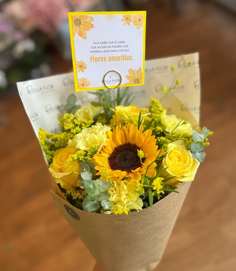 Ramo de girasol y rosas amarillas en papel kraft, con una tarjeta que dice Flores amarillas