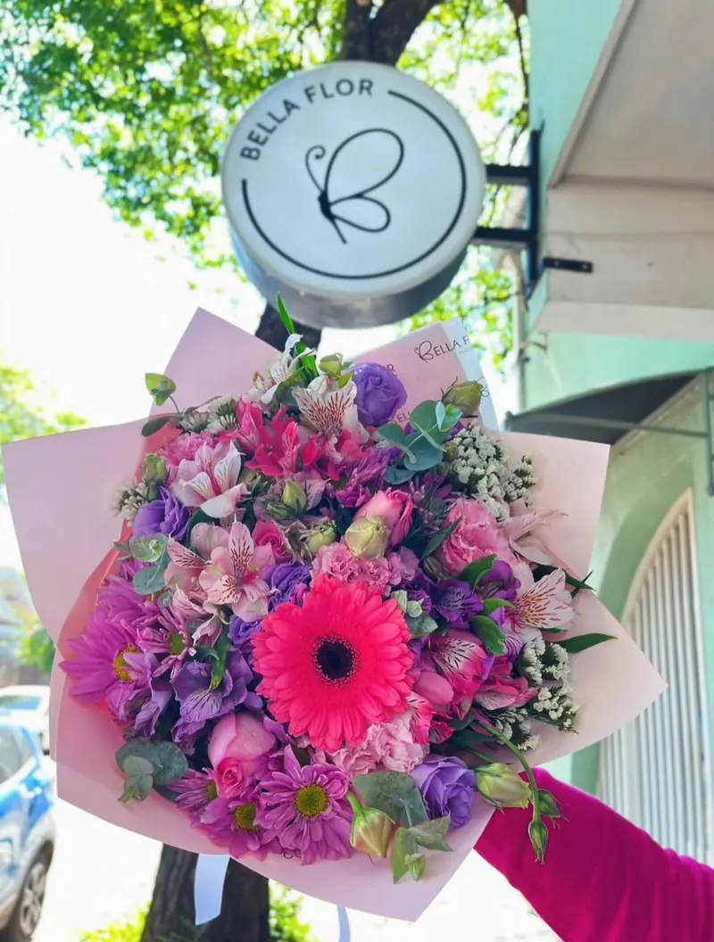 Ramo de flores rosas y violetas con una gerbera fucsia, frente al cartel redondo de Bella Flor